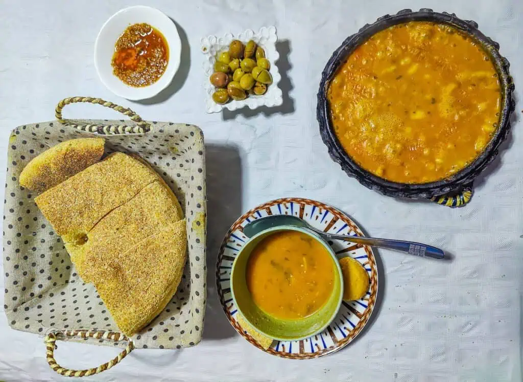 Aerial view of harira in a bowl and loubia with olives and harissa on a white table at Bab Ssour.