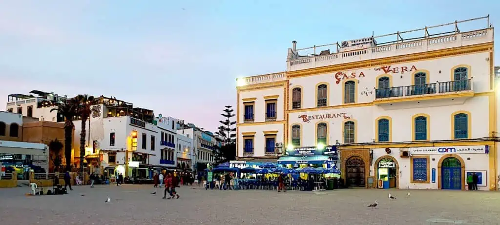 People walking through the main square in Essaouira as the sun slowly starts to set in the background.