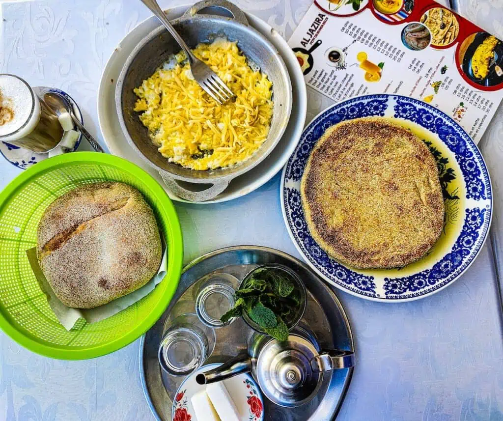Aerial view of a basket of bread and a cheese omelet and a tray with mint tea and Batbout and a coffee.