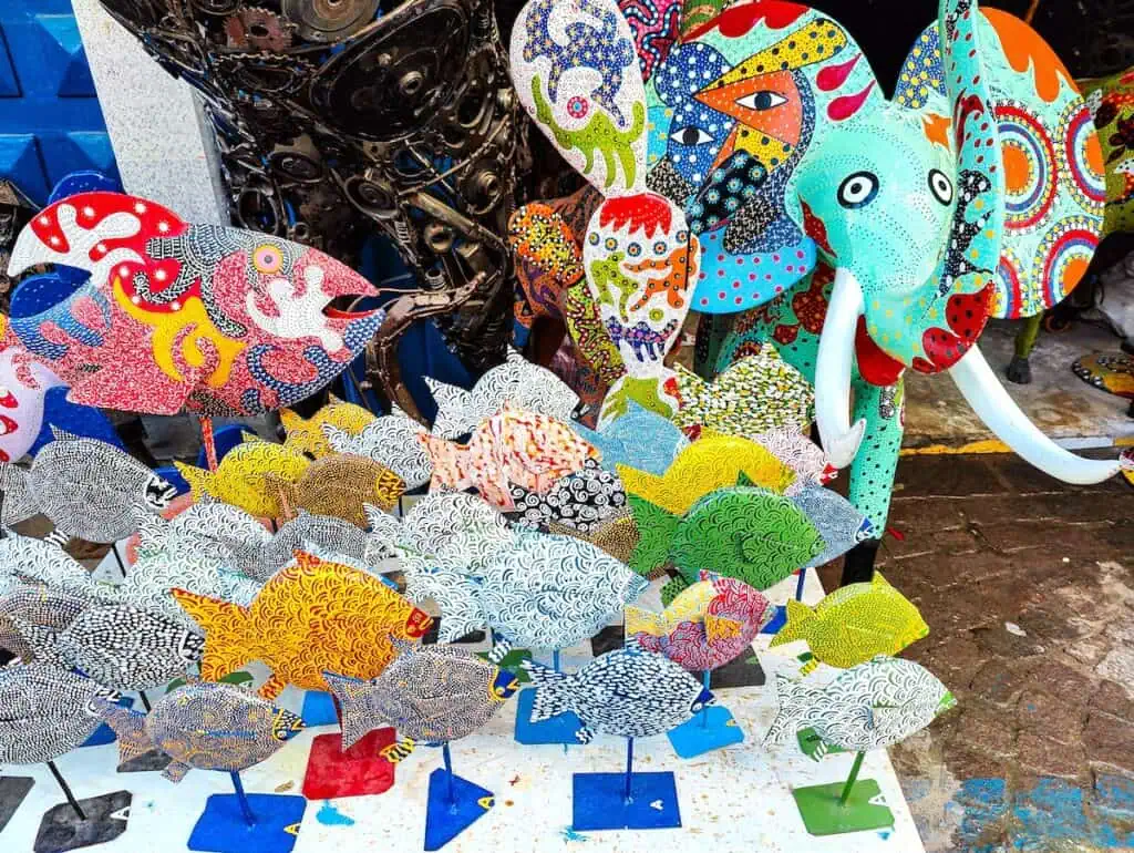 Metal fish for sale on a table in the Medina in Essaouira with a vibrant turquoise elephant with multi-color ears. When deciding on Marrakech or Essaouira, consider shopping.