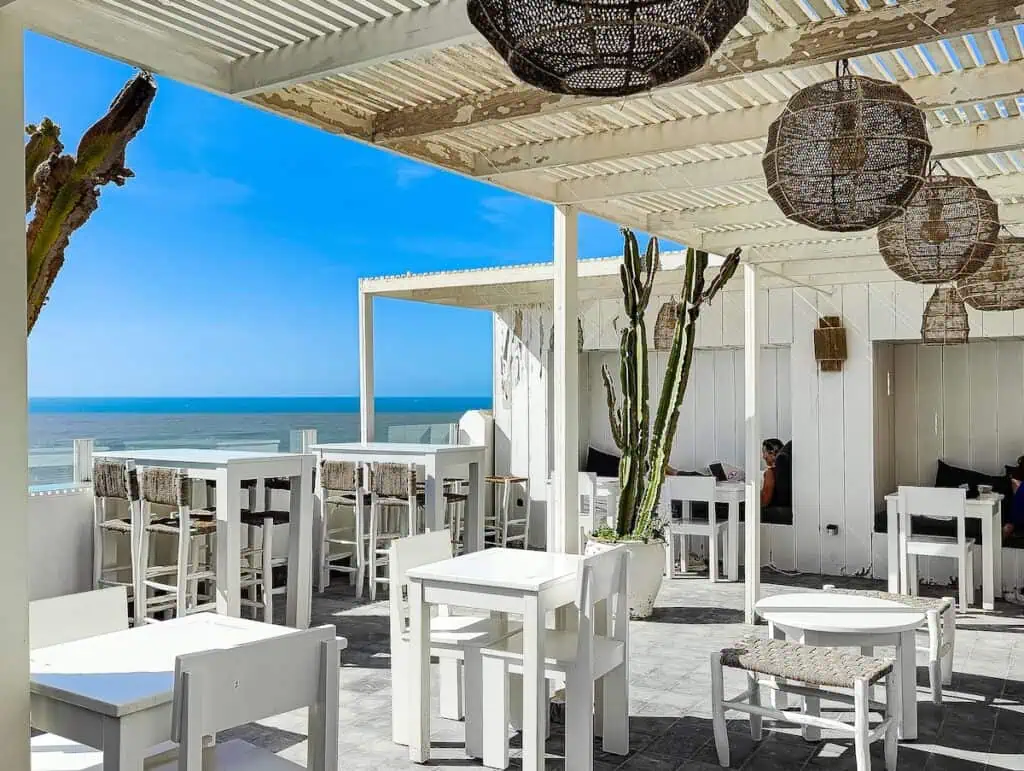 A view of the white tables and chairs on the roof of La Smala with cactus in pots and whicker lamps dangling fromt he ceiling.