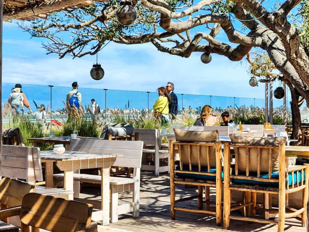 A view of white tables sitting beneath trees looking out on the beach in essaouira.