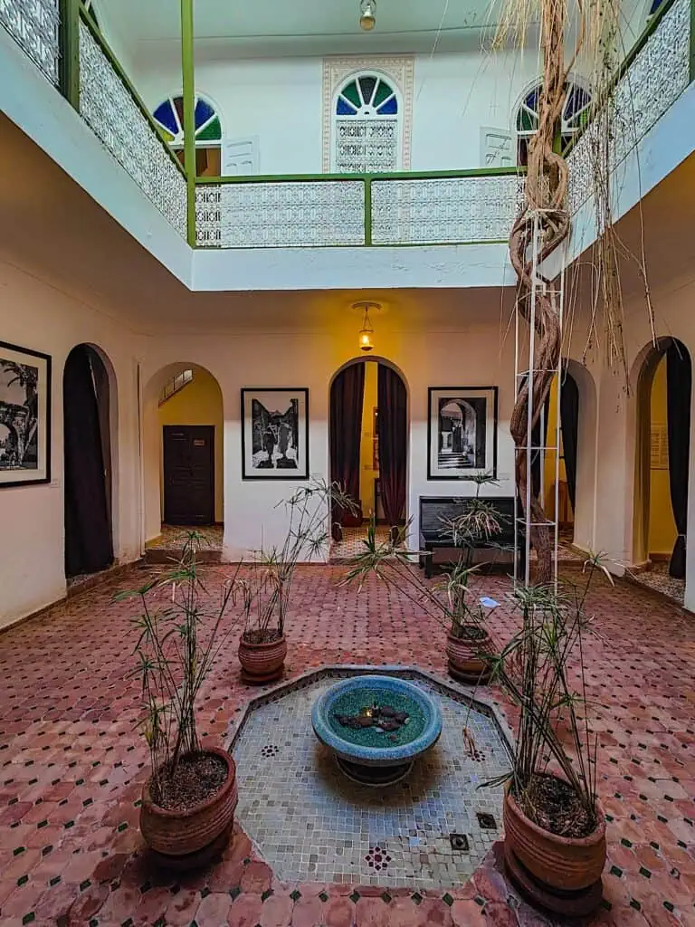 The interiior courtyard of the Maison de Photographie. It features a large courtyard with a iled courtyard and a central fountain with plants hanging around the banister.