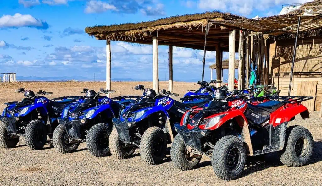 A row of blue and red quad bikes sitting in front of a wooden hut in the Agafay Desert.