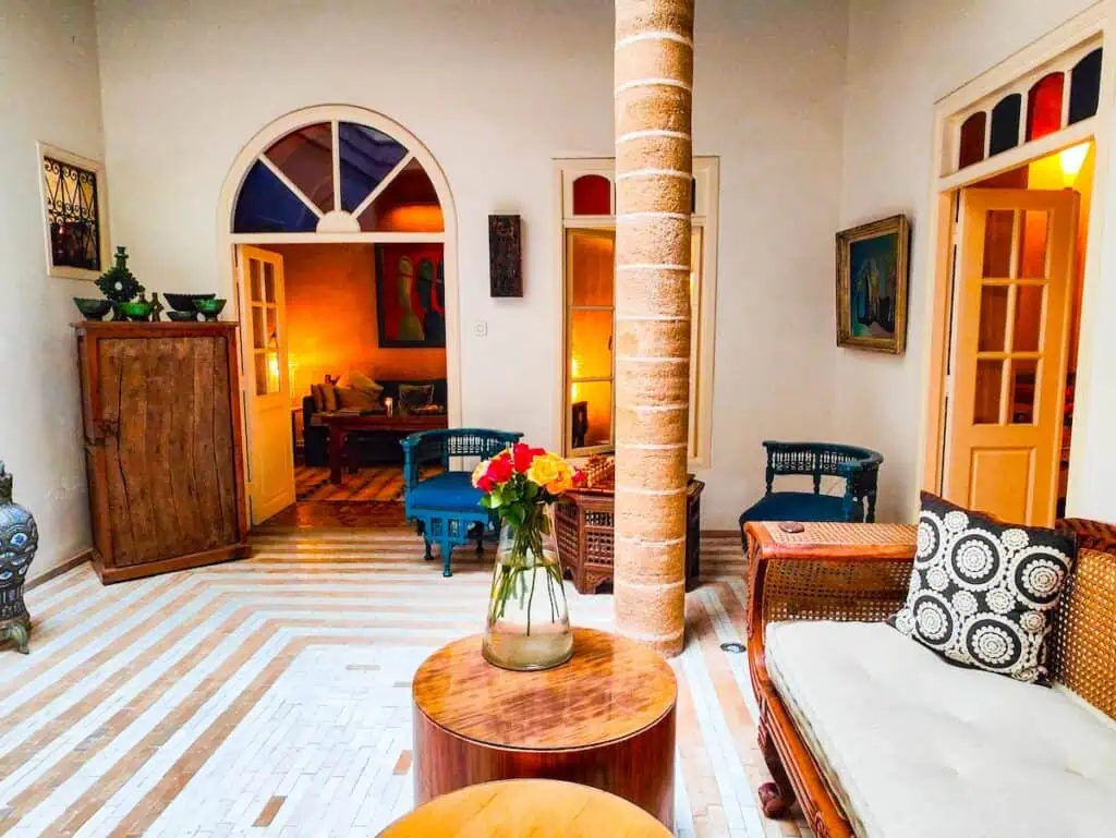 View of the light and bright lounde area in Riad Emotion. This is one of the best riads in essaouira with roud tables, multi-color windows above the doors, and modern furniture.