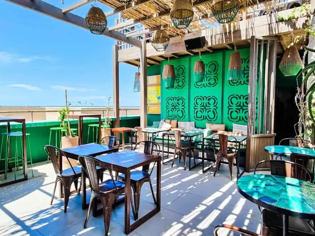 A view of an topen rooftop with tables and chairs and a green wall in the background with views of the ocean at Taros.