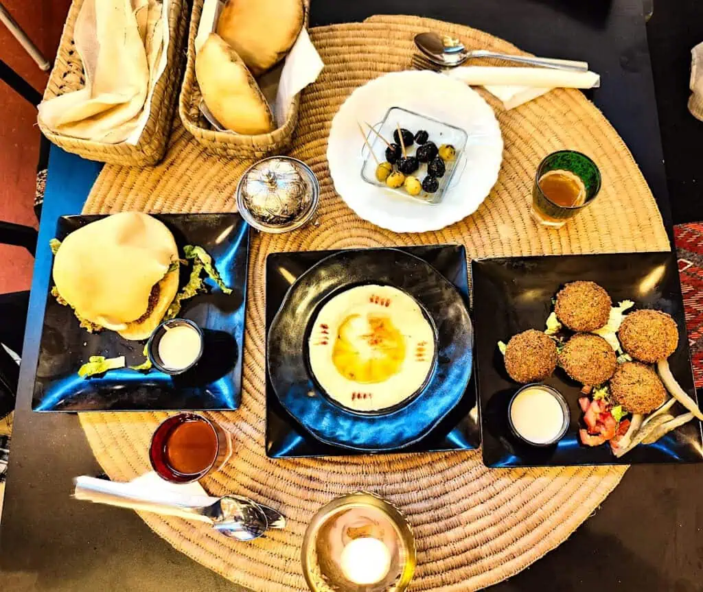 An aerial view of two baskets of bread, a bowl of olives, a plate of falafel and a falafel sandwich on a table in a restaurant.