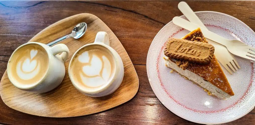 Aerial view of two lattes on a wooden tray and a piece of biscoff cheesecake on a pink plate on a wooden table at Pumpkin in essaouira.