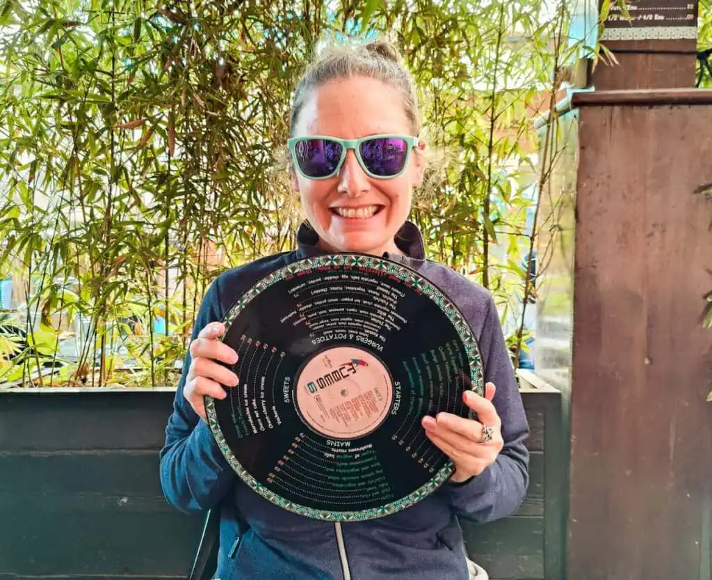 View of me holding the menu at Broc the Kasbah. I am wearing a blue, long-sleeve shirt and I am holding a vinyl record.