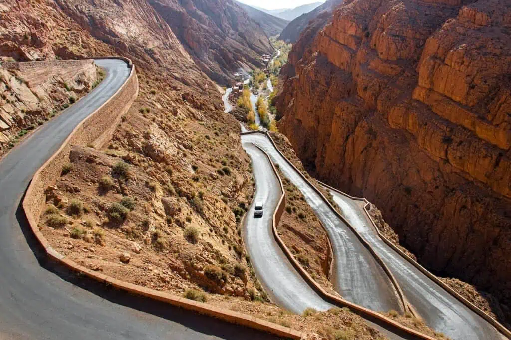 An aerial view of the zig-zagging road that takes you along the steep cliffs of Dades Gorge in Morocco. You cna see cars driving along the road in the middle of the day.