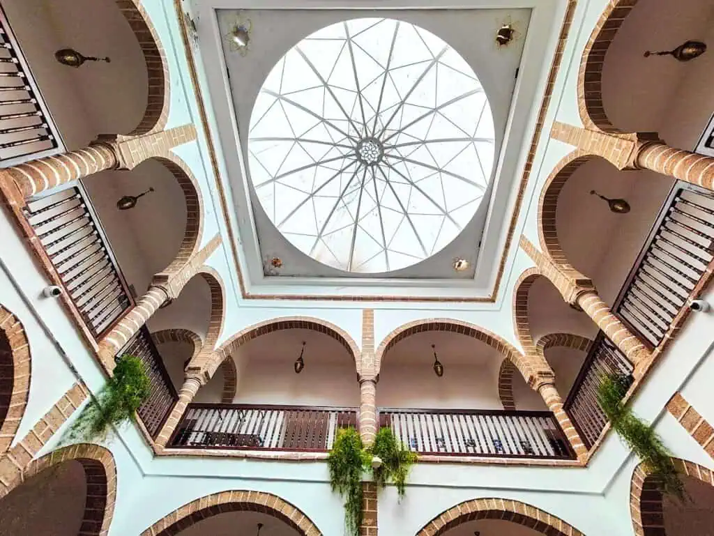 A view of the skylight inside of Dar Souiri in Essaouira. It has an open courtyard with railings and arched walls with columns and white walls.