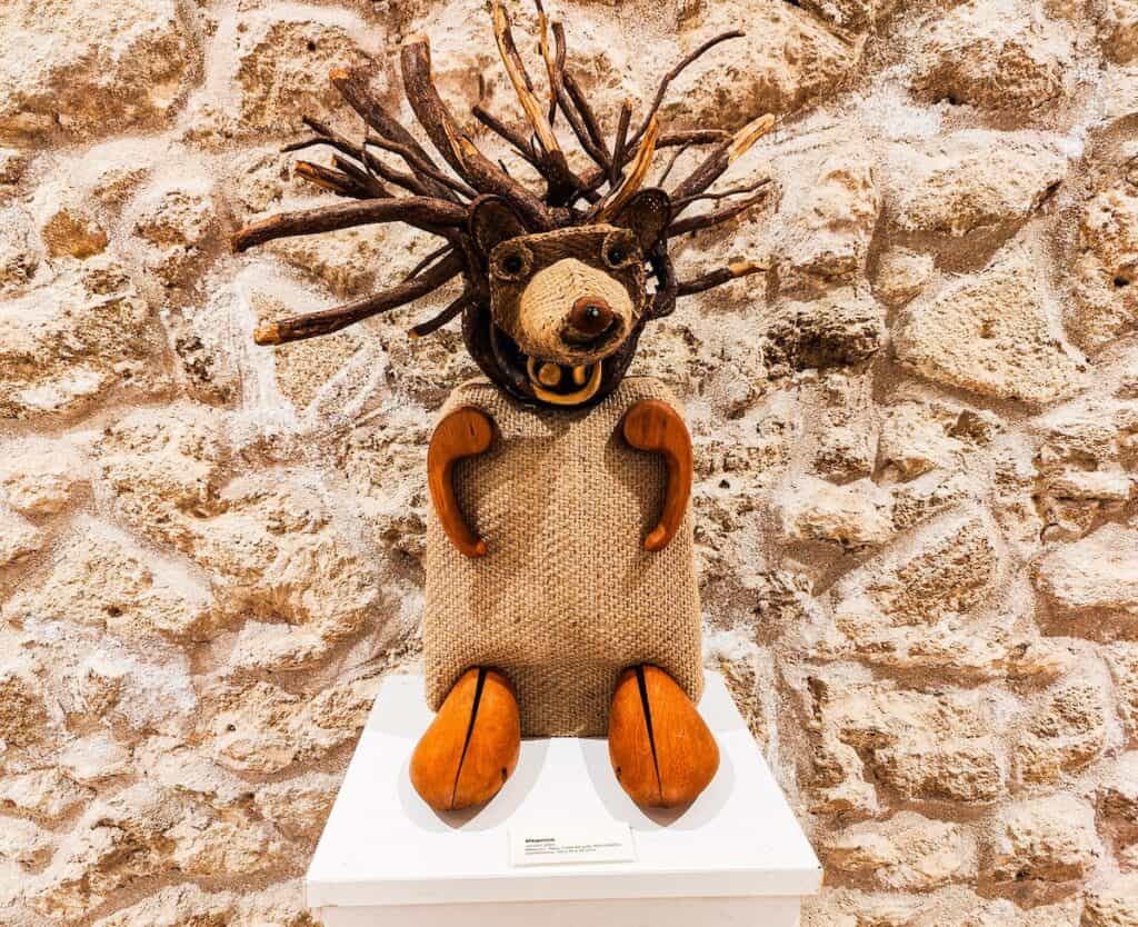 A view of a small brown bear wade of a potato sack and with atlers coming out of its head at a museum in Essaouira. It stands on a white pedestal.