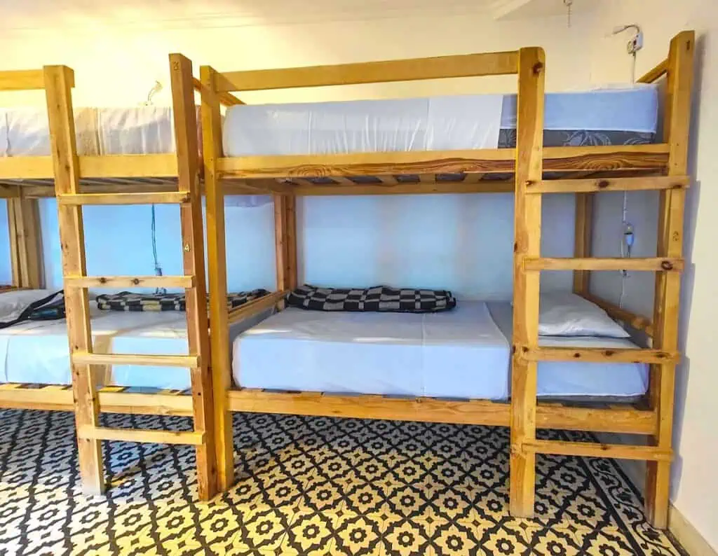 View of the wooden bunk beds with tiled floors and white sheets at Earth Hostel in Marrakech.
