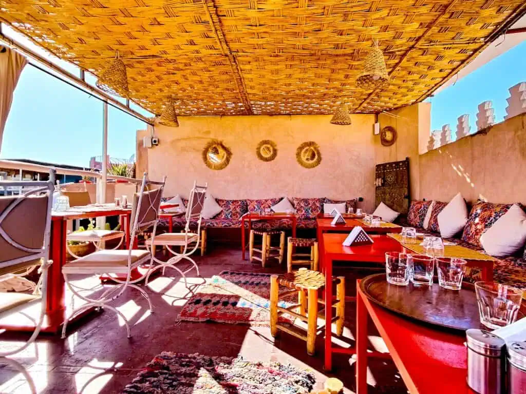 View of the thatched roof, Moroccan-inspired rooftop at Kui Zen. The tables are red and there are patterned cusions on the sofas.