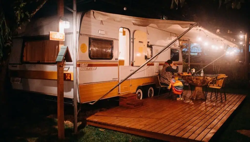 A vintage white and yellow camper all lit up in the evening. Someone is sitting outside and the porch is all lit up with an awning sitting over them. These people are enjoying some of the best camping in Essaouira.