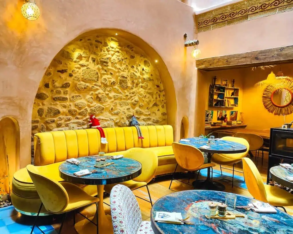 View of the restaurant in Mama Lova with round tables and chairs and a yellow couch against a wall with a arch and stone in the arch.