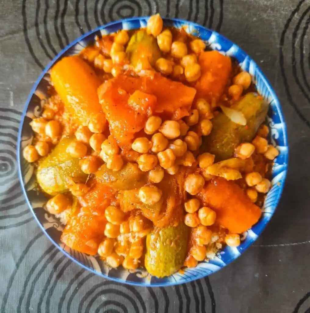 Aerial view of vegetarian couscous on a black table cloth with lots of chickpeas, veggies, and sitting inside a blue bowl. It was prepared during one of the best cooking classes in Marrakech.