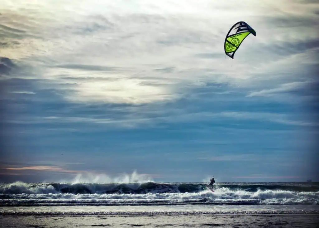 View of a kite surfer hitting the waves with a green and white kite in the air. This is one of the best things to do in Essaouira with kids.