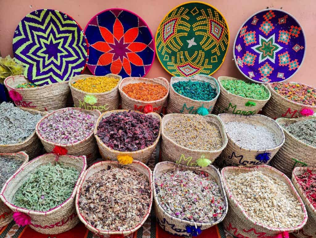 View of spices sitting in baskets in Marrakech with colorful woven "plates" in the background. You can see this during one of the best yoga retreats Marrakech has to offer.