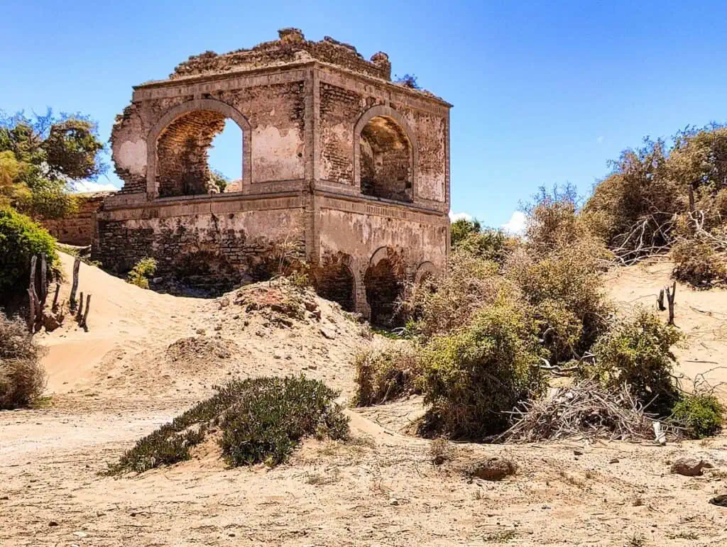 View of the ruins of an old sultan's palace in the sand in Diabat. It's a sunny day and you can see sumbling archways in an old tower that is surrounded by sand and trees. You can see this if you try the best horse riding in Essaouira.