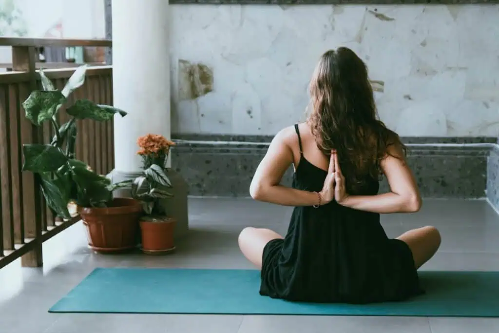 A woman wearing black sitting on a green mat with her hands behind her back. She hasd long borwn hair and is sitting in a yoga studio with white walls. She is enjoying the best yoga in Essaouira Morocco.