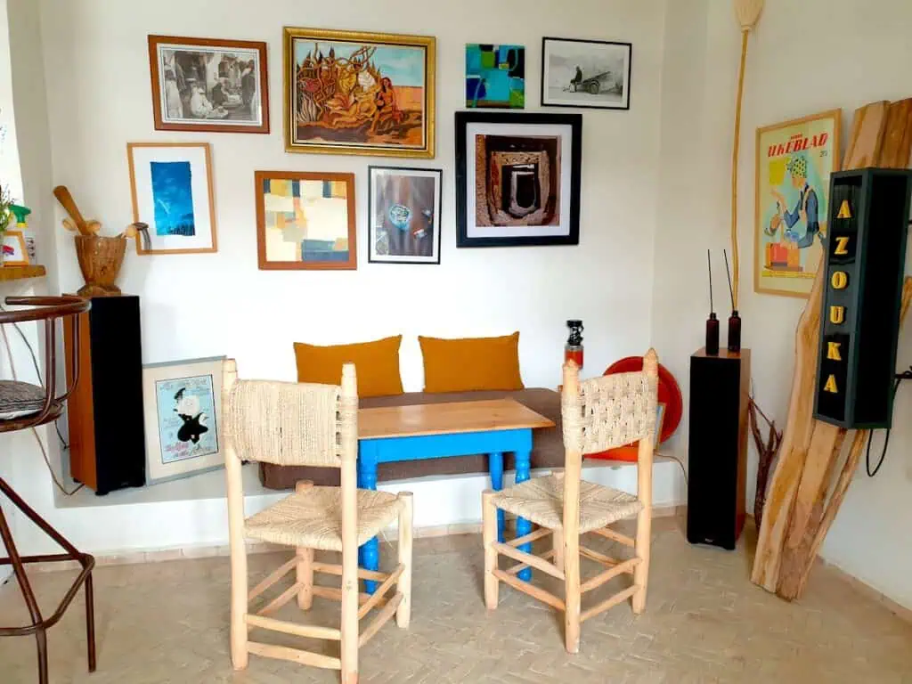 Cpzy interior of Azouka Eatery. You can see pictures hanging on a white wall above a small table with a banquet and borwn pillows.