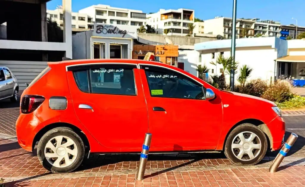 View of an orange hatchback cab sitting on the street in Agadir on a sunny day. When deciding on Agadir or Essaouira, remmeber that you need to use transportation to get around Agadir.