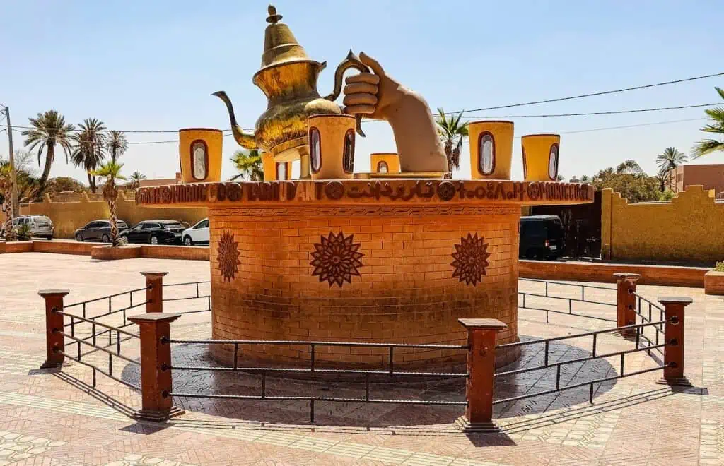 View of a giant hand holding a gold tea pot surrounded by a fence and on a pedistal in Taroudant.