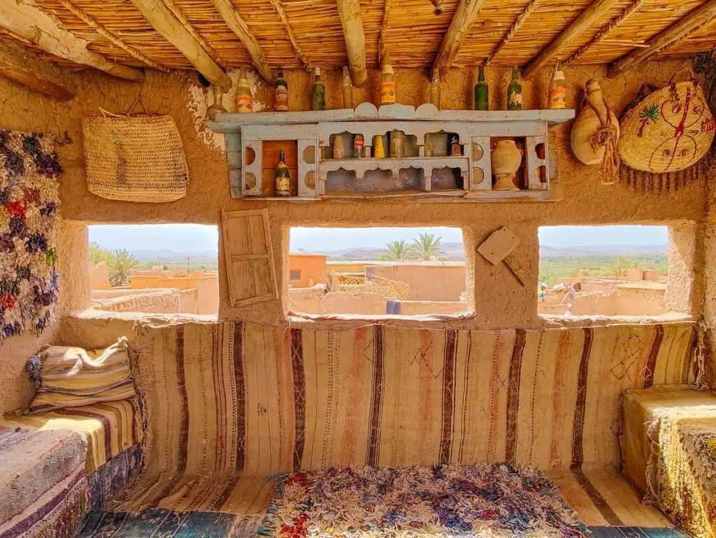 View of a historic rooftop in Ouarzate. You can see the surrounding buildings through small windows and two benches on either side. You can also see knick-knacks on the wall. You could do a day trip here in Marrakech in May.