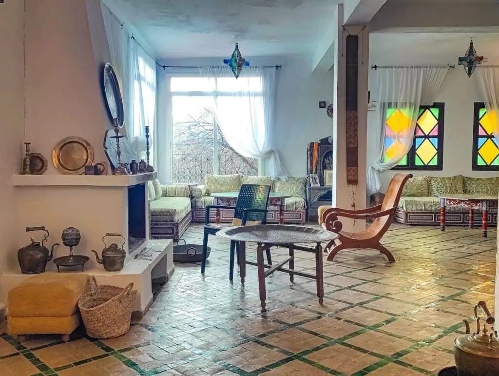 View of the Moroccan-style sitting area with chairs and tables and knick knacks and stained glass windows.