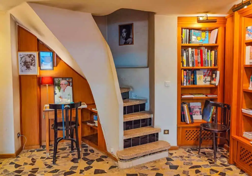 View of the interior of this Tangier bookstore. Table about wooden book shelves and a spiral staircase in the center.