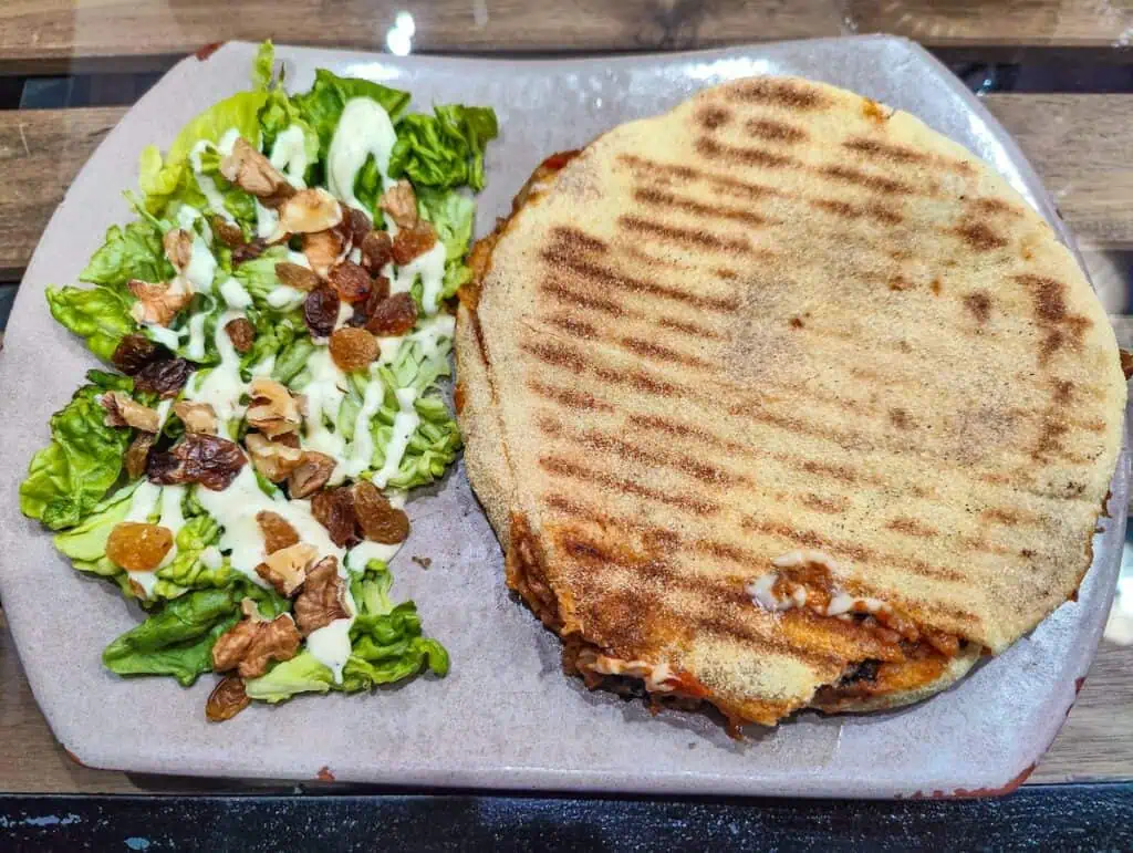View of an eggplant panini with a small salad on the side with nuts, dried fruit, and a white salad dressing.