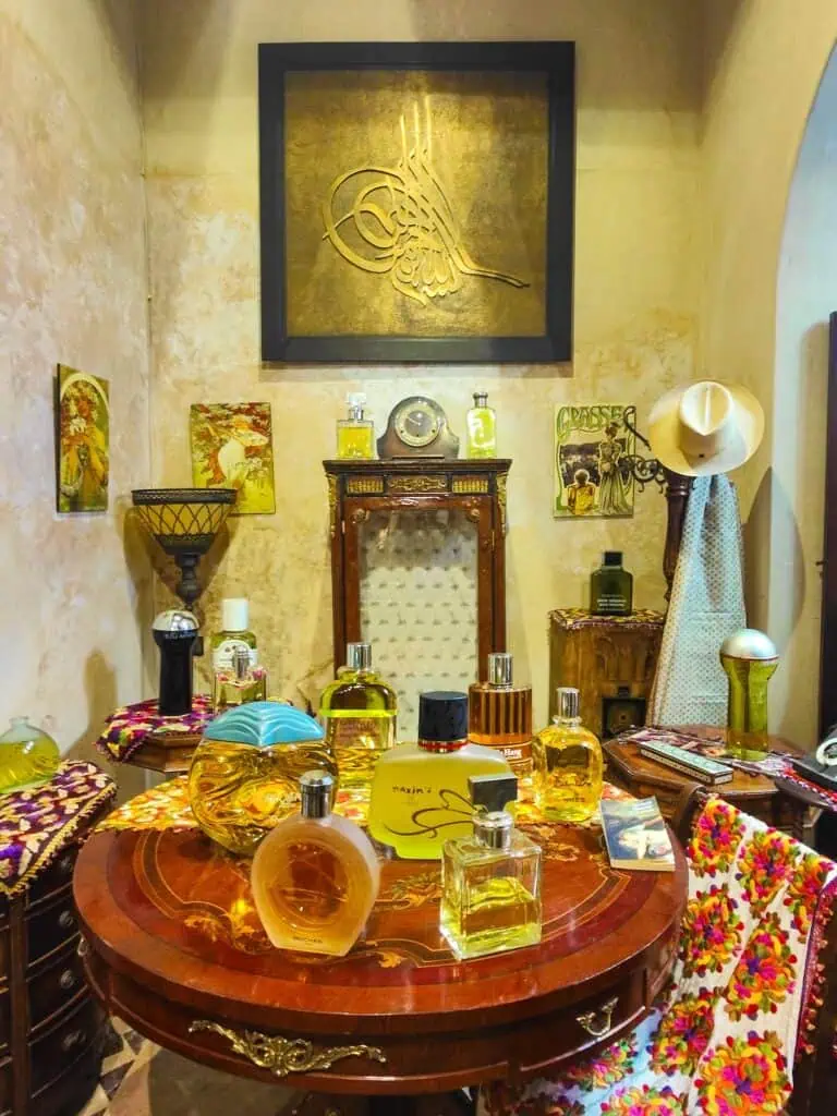 Vintahe perfumes displayed on a round wooden table with antiques in the background.