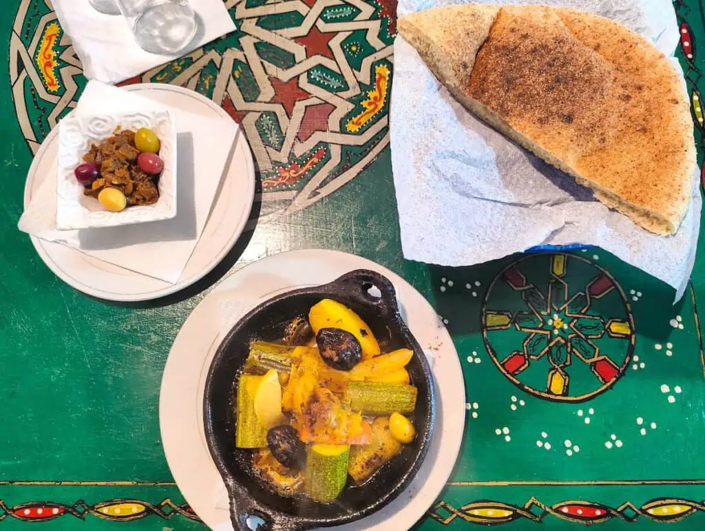 Aerial view of bread, olives, eggplant, and tajine in an iron skillet.